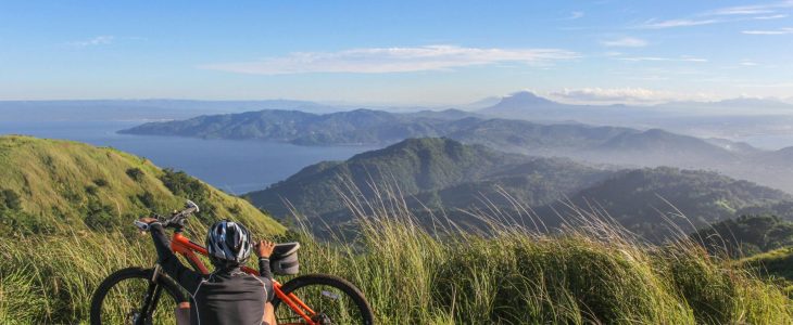 Person sitting on a hillside next to a bike looking into the distance