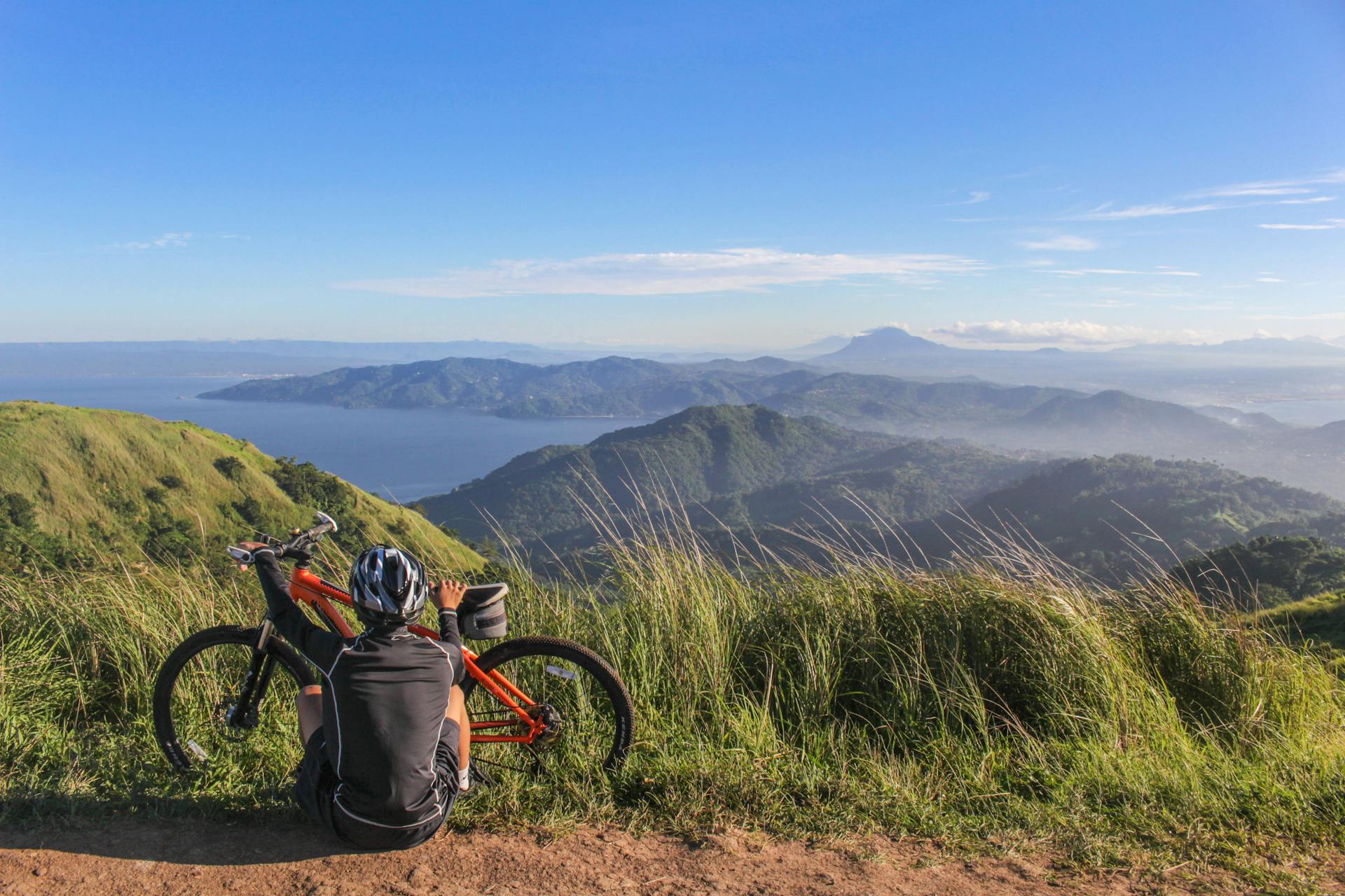 Person sitting on a hillside next to a bike looking into the distance